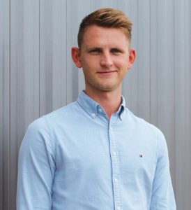 Ansprechpartner Andreas Neu trägt ein hellblaues Hemd und wurde frontal vor einem grauen Trapezblech im Hintergrund fotografiert.